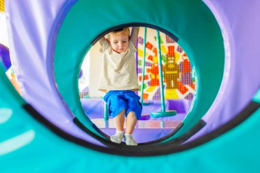 Şirin küçük çocuk, kapalı eğlence parkındaki renkli oyun bahçesinde sürünüyor ve oynuyor.