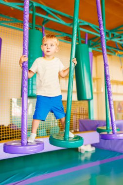 Şirin küçük çocuk, kapalı eğlence parkındaki renkli oyun bahçesinde sürünüyor ve oynuyor.