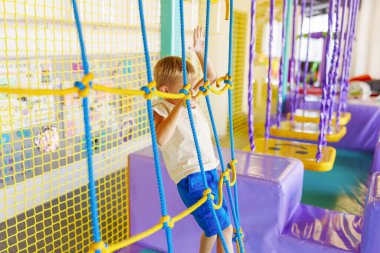 Şirin küçük çocuk, kapalı eğlence parkındaki renkli oyun bahçesinde sürünüyor ve oynuyor.