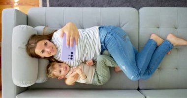 Kadın ve küçük oğlu akıllı telefonuyla rahat bir kanepede uzanmış, manzaranın üstünde. Aileler evde birlikte vakit geçirirler. Akıllı telefon kullanır, oyun oynar, video izler, selfie çekerler. Yüksek kalite 4k görüntü