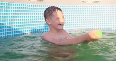 Çocuk güneşli yaz gününde havuzda su tabancasıyla oynar, havuz eğlencesi. Yüksek kalite 4k görüntü