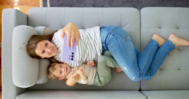 Mujer Pequeño Hijo Tumbados Acogedor Sofá Con Smartphone Por Encima — Vídeos de Stock