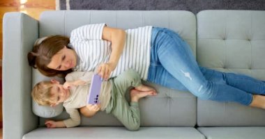 Kadın ve küçük oğlu akıllı telefonuyla rahat bir kanepede uzanmış, manzaranın üstünde. Aileler evde birlikte vakit geçirirler. Akıllı telefon kullanır, oyun oynar, video izler, selfie çekerler. Yüksek kalite 4k görüntü