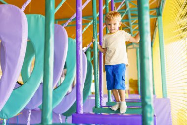 Şirin küçük çocuk, kapalı eğlence parkındaki renkli oyun bahçesinde sürünüyor ve oynuyor.