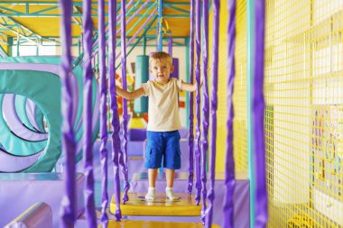 Şirin küçük çocuk, kapalı eğlence parkındaki renkli oyun bahçesinde sürünüyor ve oynuyor.