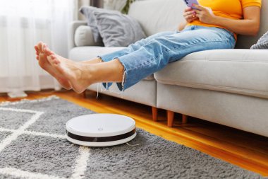 Kadın evdeki kanepede dinlenirken robot süpürgesi odayı temizliyor..