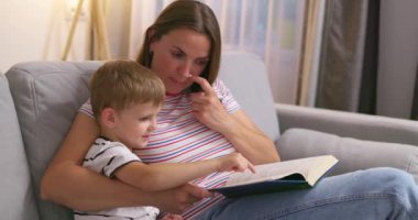 Anne ve oğlu oturma odasındaki rahat bir kanepede oturmuş kitap okuyorlar, ailecek. Yüksek kalite 4k görüntü
