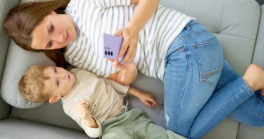 Kadın ve küçük oğlu akıllı telefonuyla rahat bir kanepede uzanmış, manzaranın üstünde. Aileler evde birlikte vakit geçirirler. Akıllı telefon kullanır, oyun oynar, video izler, selfie çekerler. Yüksek kalite 4k görüntü