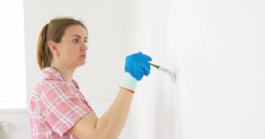 Bir kadın odada tamirat yapar. Bir kız boya fırçasıyla bir duvarı beyaza boyuyor. Odada onarım var. Yenileme. Yüksek kalite 4k görüntü