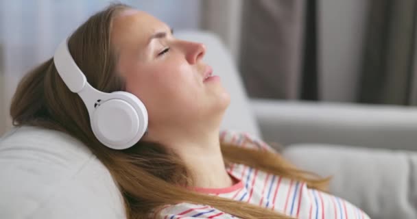 헤드폰을 편안한 소파에서 휴식을 취하는 소녀는 집에서 휴식을 음악과 오디오 — 비디오