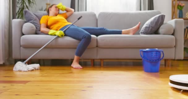 一定の掃除に疲れた女性は快適なソファーに横たわり ロボット掃除機は掃除を行います クリーニングのための革新的な技術 高品質の4K映像 — ストック動画