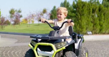 Bir yaz günü parkta oyuncak elektrikli araba kullanan bir çocuk. Bir çocuk elektrikli dörtlü bisiklet sürüyor. Yüksek kalite 4k görüntü