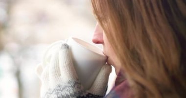 Beyaz eldiven giymiş hoş bir kadın kışın açık havada sıcak çikolata, çay ya da kahve içer. Yüksek kalite 4k görüntü