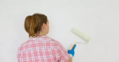 Bir kadın odada tamirat yapar. Bir kız beyaz bir silindirle bir duvar boyuyor. Odada onarım var. Yenileme. Yüksek kalite 4k görüntü