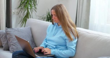 Genç kadın kanepede oturmuş dizüstü bilgisayarla mesaj yazarken, bilgisayarla sohbet ederken, internette gezinirken sosyal medyada çalışırken ya da evde çalışırken