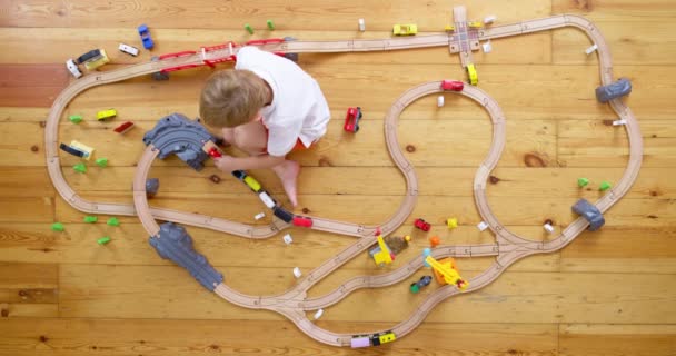 自宅や幼稚園で床に玩具の木製鉄道で遊んでいるかわいい子供 木製の教育玩具 トップビュー 高品質の4K映像 — ストック動画