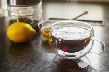 Bir fincan sıcak siyah çay, bir kase ballı ve limonlu ahşap masa.