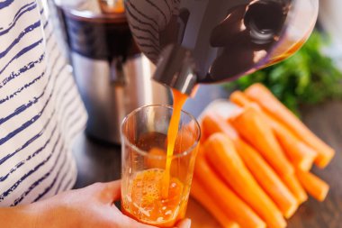 A woman pours fresh carrot juice into glass. Freshly squeezed carrot juice using a juicer clipart