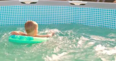 Çocuk arka bahçedeki havuzda eğleniyor, şişme kucağa mutlu bir şekilde sıçrıyor. Yüksek kalite 4k görüntü