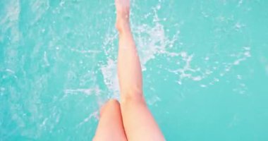 Çıplak ayaklı, güneşlenen, açık havuz manzaralı, saf suda ayaklarıyla oynayan bir kadın. Yüksek kalite 4k görüntü