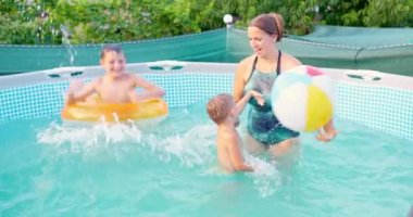 Anne ve iki oğlu gülüyor, yüzüyor, yaz havuzunda su sıçratıyorlar, yaz tatilinde eğleniyorlar. Yüksek kalite 4k görüntü