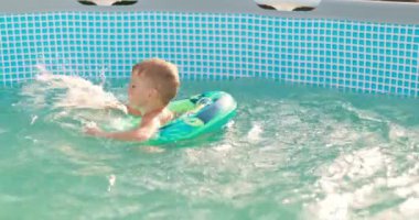 Çocuk arka bahçedeki havuzda eğleniyor, şişme kucağa mutlu bir şekilde sıçrıyor. Yüksek kalite 4k görüntü