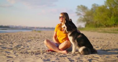 Mutlu hayvan sahibi yazın sahilde köpeğini kucaklıyor ve dinleniyor. Evcil köpeğiyle gezmekten hoşlanan bir kadın. Yüksek kalite 4k görüntü