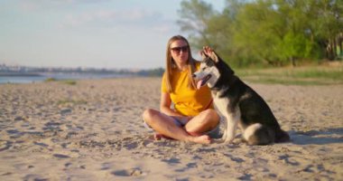 Mutlu hayvan sahibi yazın sahilde köpeğini kucaklıyor ve dinleniyor. Evcil köpeğiyle gezmekten hoşlanan bir kadın. Yüksek kalite 4k görüntü
