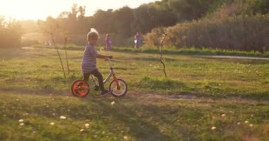 Bir çocuk şehir parkında dengeli bisiklet sürüyor. Bisiklete binen mutlu çocuk, doğada eğleniyor. Aktif aile eğlencesi. Yüksek kalite 4k görüntü