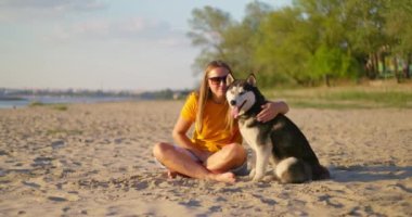 Mutlu hayvan sahibi yazın sahilde köpeğini kucaklıyor ve dinleniyor. Evcil köpeğiyle gezmekten hoşlanan bir kadın. Yüksek kalite 4k görüntü