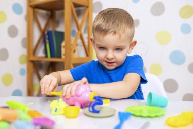 Küçük çocuk coşkuyla plasticinle oynuyor, evde beyaz masada hamur oynuyor, çocukların yaratıcılık kavramı. İnce motor becerilerin gelişimi