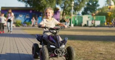 Bir yaz günü parkta oyuncak elektrikli araba kullanan bir çocuk. Bir çocuk elektrikli dörtlü bisiklet sürüyor. Yüksek kalite 4k görüntü