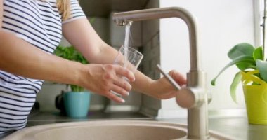 Kadın mutfaktaki bardaktan temiz filtrelenmiş su döküyor. Saf içme suyu kavramı. Yüksek kalite 4k görüntü