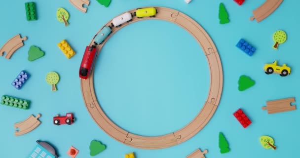 带有汽车的玩具木制火车在蓝色背景的铁路上穿梭于儿童玩具之上 复制空间 玩具商店或开发游戏中心的广告 顶部视图 高质量的4K镜头 — 图库视频影像