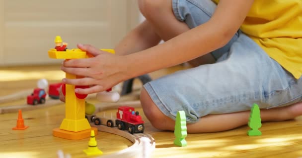 少年は子供の鉄道で遊んでいる 子供は床に木製のおもちゃで遊んでいる おもちゃ列車は木製の鉄道に乗っています 高品質の4K映像 — ストック動画