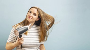 Açık mavi arka planda saç kurutma makinesi kullanan güzel bir genç kadın. Saç bakımı ve güzellik. Günlük hijyen konsepti