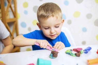 Küçük çocuk coşkuyla plasticinle oynuyor, evde beyaz masada hamur oynuyor, çocukların yaratıcılık kavramı. İnce motor becerilerin gelişimi