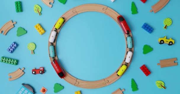两列木制玩具火车 车子在蓝色背景的圆形铁路上行驶 还有儿童玩具 复制空间 顶部视图 高质量的4K镜头 — 图库视频影像