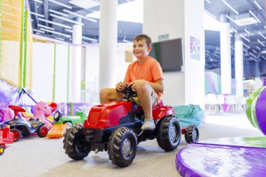 Bir çocuk çocuk oyun merkezinde oyuncak pedallı arabaya biniyor..