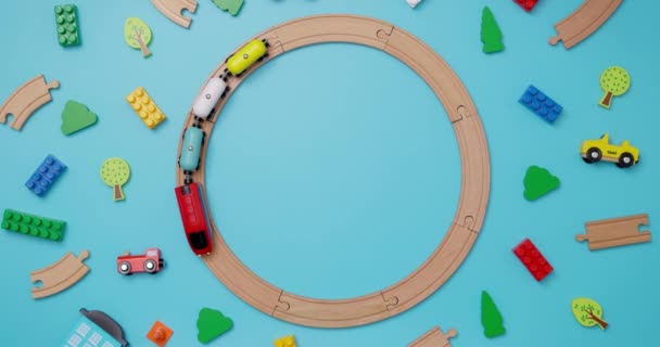 带有汽车的玩具木制火车在蓝色背景的铁路上穿梭于儿童玩具之上 复制空间 玩具商店或开发游戏中心的广告 顶部视图 高质量的4K镜头 — 图库视频影像