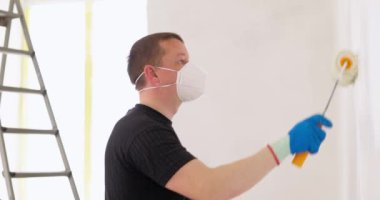 Duvarı beyaz boyayla boyayan adam paten fırçası kullanıyor. Yenileme evi. Yeniden dizayn et ve yeni evini geliştir. Yüksek kalite 4k görüntü