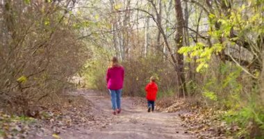 Güneşli bir sonbahar gününde anne ve oğlu ormanda yürüyor. Yürüyüş, temiz hava, sağlık, yürüyüş ve keşif. Açık hava aktiviteleri. Yüksek kalite 4k görüntü