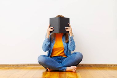 Genç bir kadın duvara yaslanmış bir kitapla yüzünü kapatıyor..