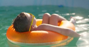 Sarı güneş gözlüklü bir çocuk şişme halkada havuzda dinleniyor. Mutlu çocuk yaz tatilini şişme yüzükle bilardo oynayarak geçiriyor. Yaz tatili. Yüksek kalite 4k görüntü