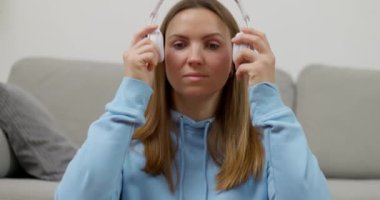 Bir kadın evindeki oturma odasında lotus poz verirken kendini meditasyon sürecine tamamen sokmak için kulaklık takıyor. Yüksek kalite 4k görüntü