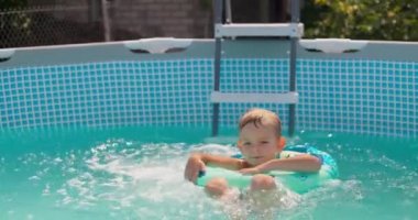 Şişme yüzüklü küçük mutlu çocuk havuzda eğleniyor, gülüyor ve dışarı sıçrıyor. Yaz tatili, tatil. Açık hava aktiviteleri. Yüksek kalite 4k görüntü