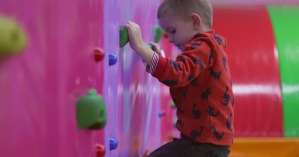 小さな男の子がトランポリン公園の登山壁を登ります エンターテイメント スポーツ 屋内遊び場 高品質の4K映像 — ストック動画