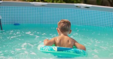 Şişme yüzüklü küçük mutlu çocuk havuzda eğleniyor, gülüyor ve dışarı sıçrıyor. Yaz tatili, tatil. Açık hava aktiviteleri. Yüksek kalite 4k görüntü