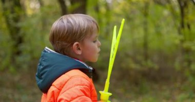 Sonbahar parkında sabun köpüğüyle oynayan mutlu beyaz çocuk. Doğada eğlenen küçük bir çocuk. Yüksek kalite 4k görüntü