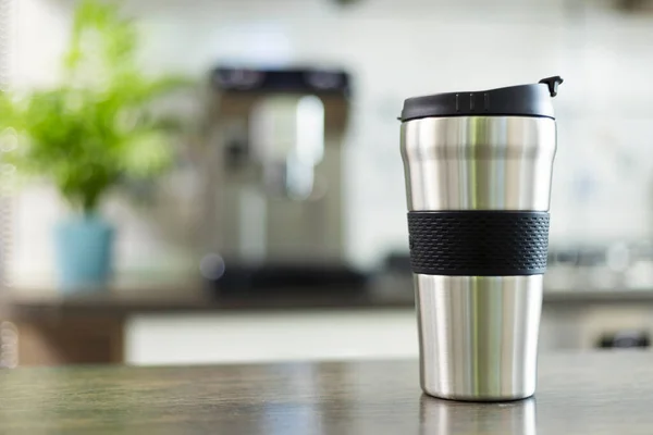 A sleek stainless steel travel mug with a black grip stands ready on a kitchen counter, showcasing the modern on-the-go lifestyle.